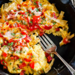 Overhead view of migas topped with chopped tomatoes and melted cheese in a cast iron skillet.