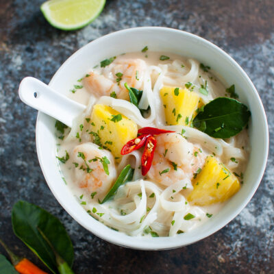 Bowl of Thai coconut soup with shrimp, pineapples, and flat noodles.