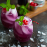 Glass of hibiscus tea cocktail garnished with mint and a maraschino cherry.