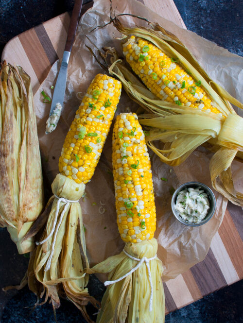 Grilled corn on a wooden board with a small bowl of compound butter.