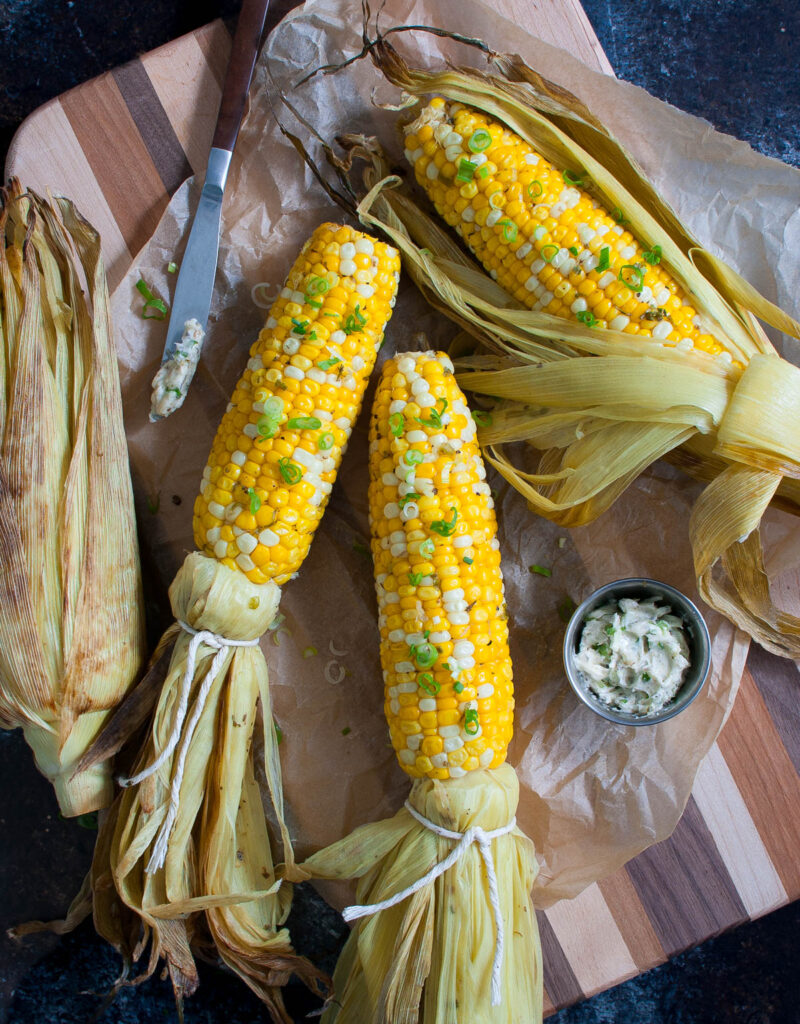 Grilled corn on a wooden board with a small bowl of compound butter.