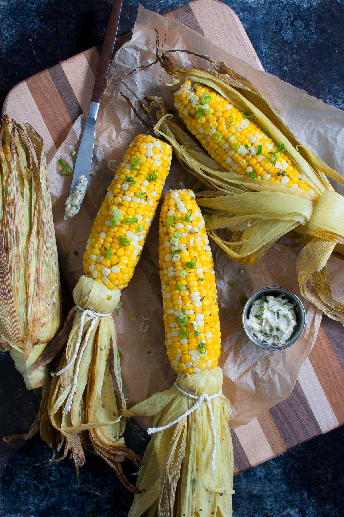 Grilled corn on a wooden board with a small bowl of compound butter.