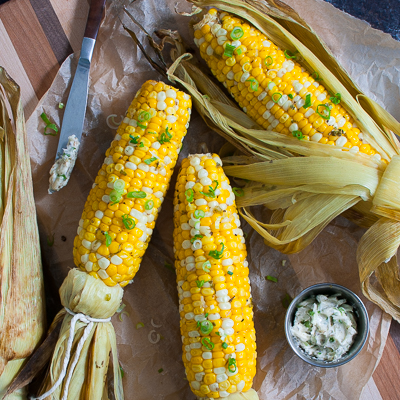 Grilled corn on a wooden board with a small bowl of compound butter.