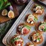 Overhead view of tray of pancetta crisps topped with goat cheese, figs, and baby arugula.