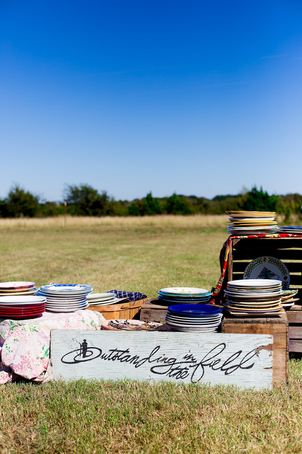 A stack of dishes behind the Outstanding in the Field wooden sign.