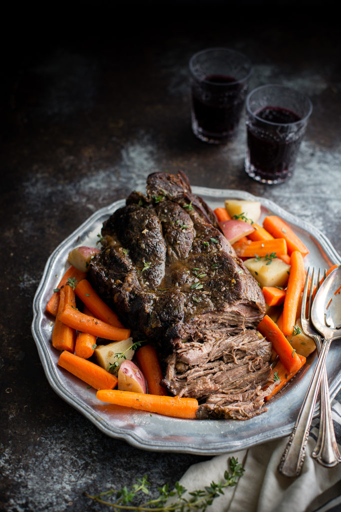 A pot roast on a serving platter with carrots and potatoes.
