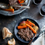 A serving of pot roast, carrots, and potatoes on a black plate.