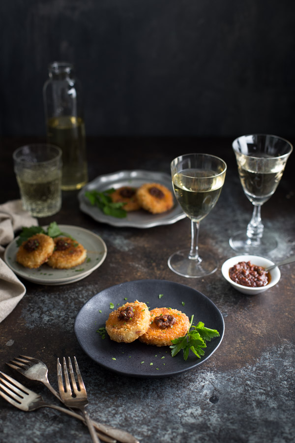 A tabletop with several small plates of risotto cakes and glasses of wine.