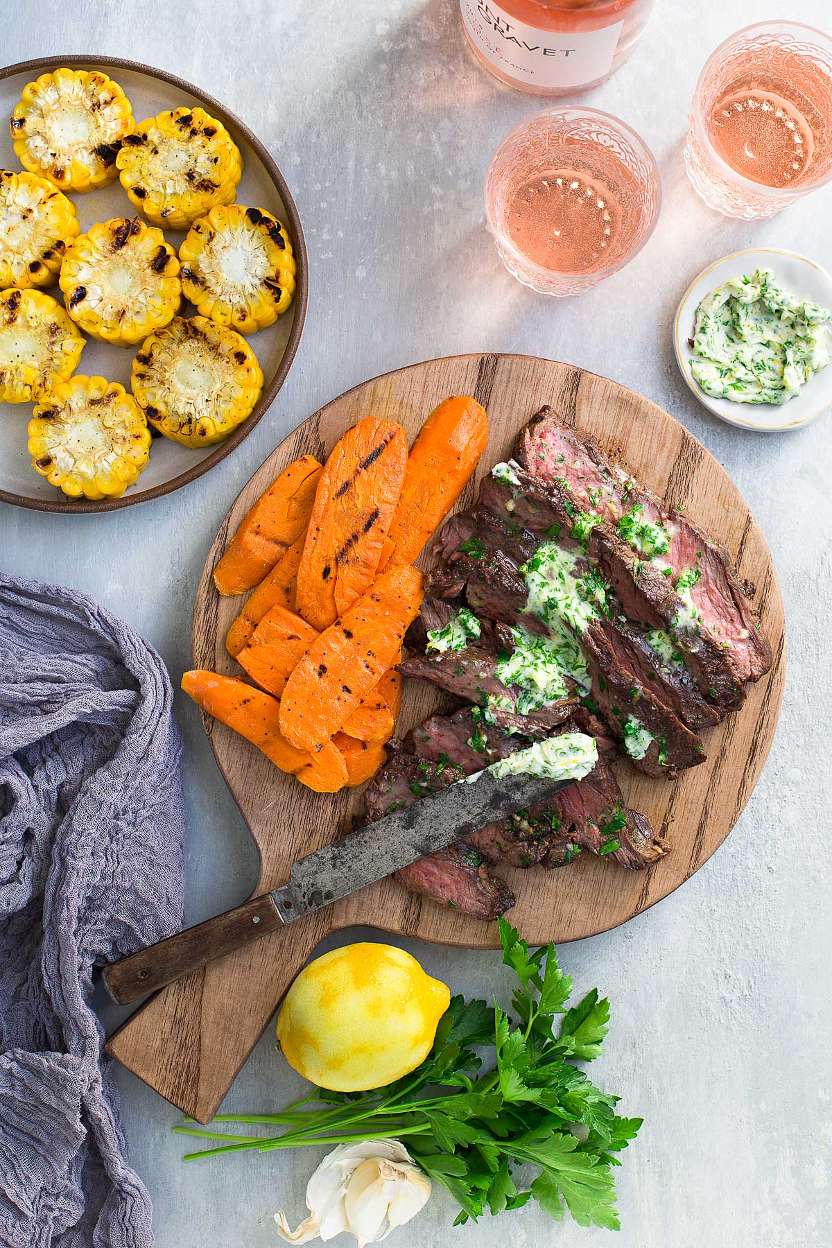 Steak slices topped with parsley-lemon-garlic butter on a cutting board and served with grilled vegetables.