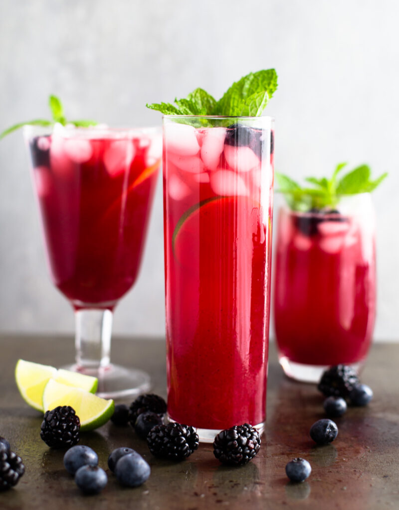 Three glasses of blackberry-blueberry lemonade garnished with mint sprigs.