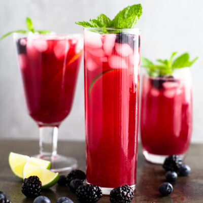Three glasses of blackberry-blueberry lemonade garnished with mint sprigs.
