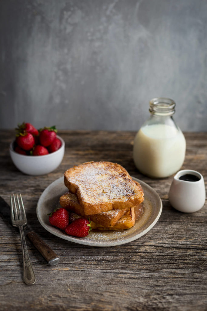 Slices of french toast dusted with powdered sugar served with strawberries.