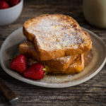 Slices of french toast dusted with powdered sugar served with strawberries.