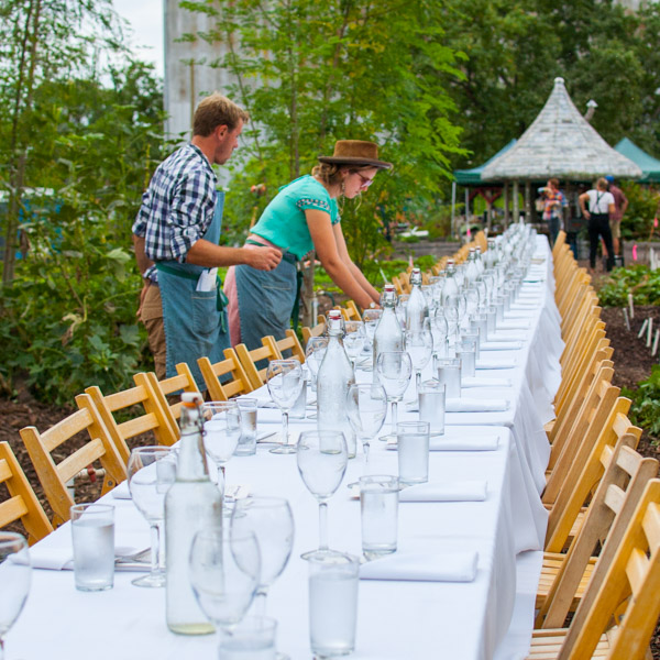 Two people setting a table with wine glasses outside.