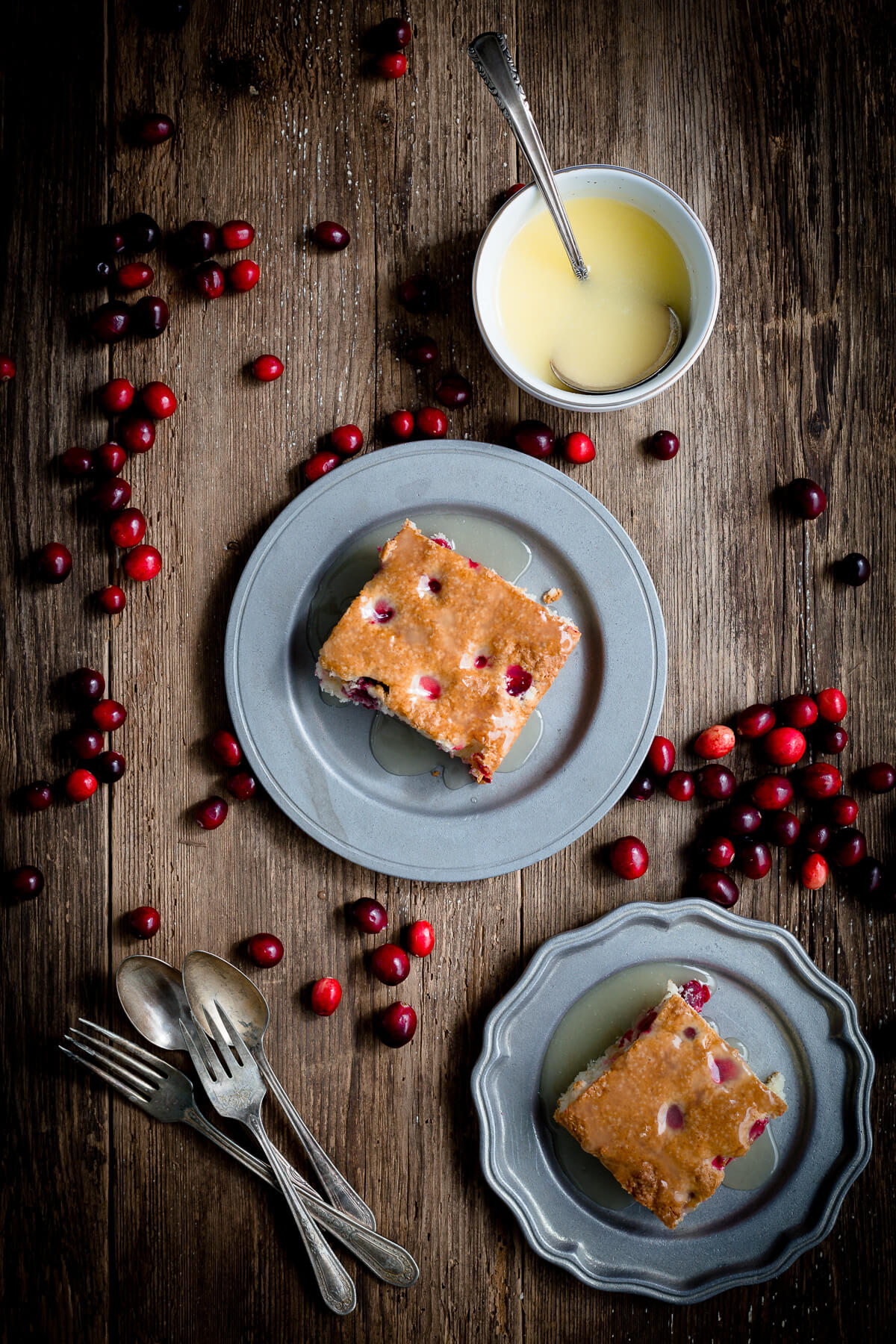 Overhead view of two servings of cranberry pudding cake with warm butter sauce and bowl of sauce.