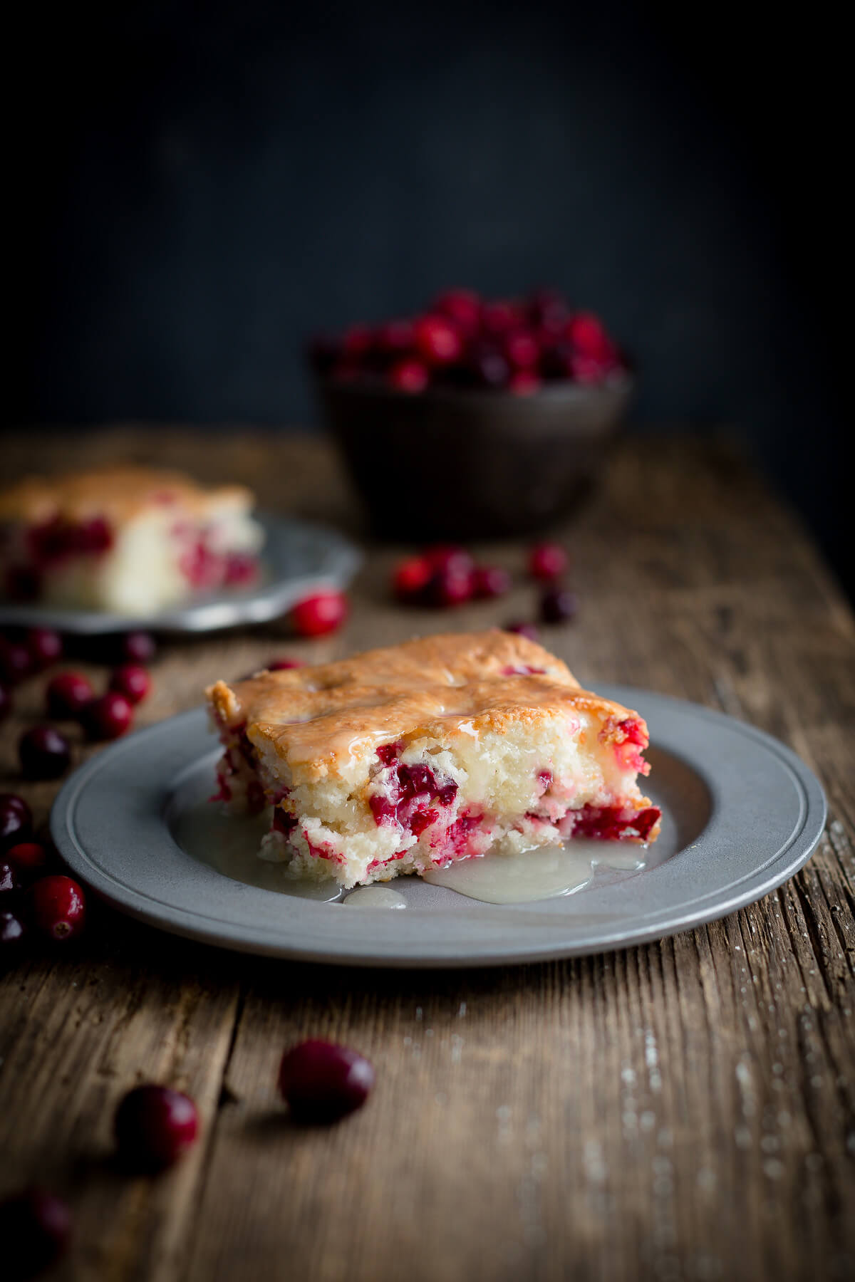 Serving of cranberry pudding cake topped with warm butter sauce on a pewter plate on wooden background.