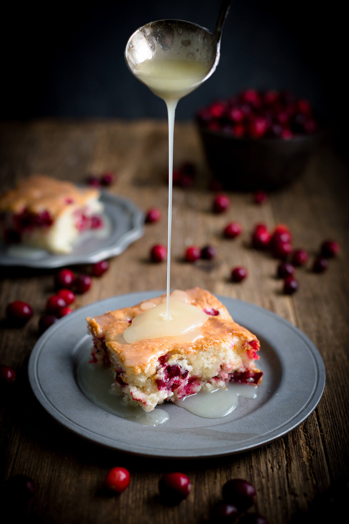 Serving of cranberry pudding cake on a pewter plate with warm butter sauce being poured on it.