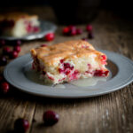 Serving of cranberry pudding cake topped with warm butter sauce on a pewter plate on wooden background.