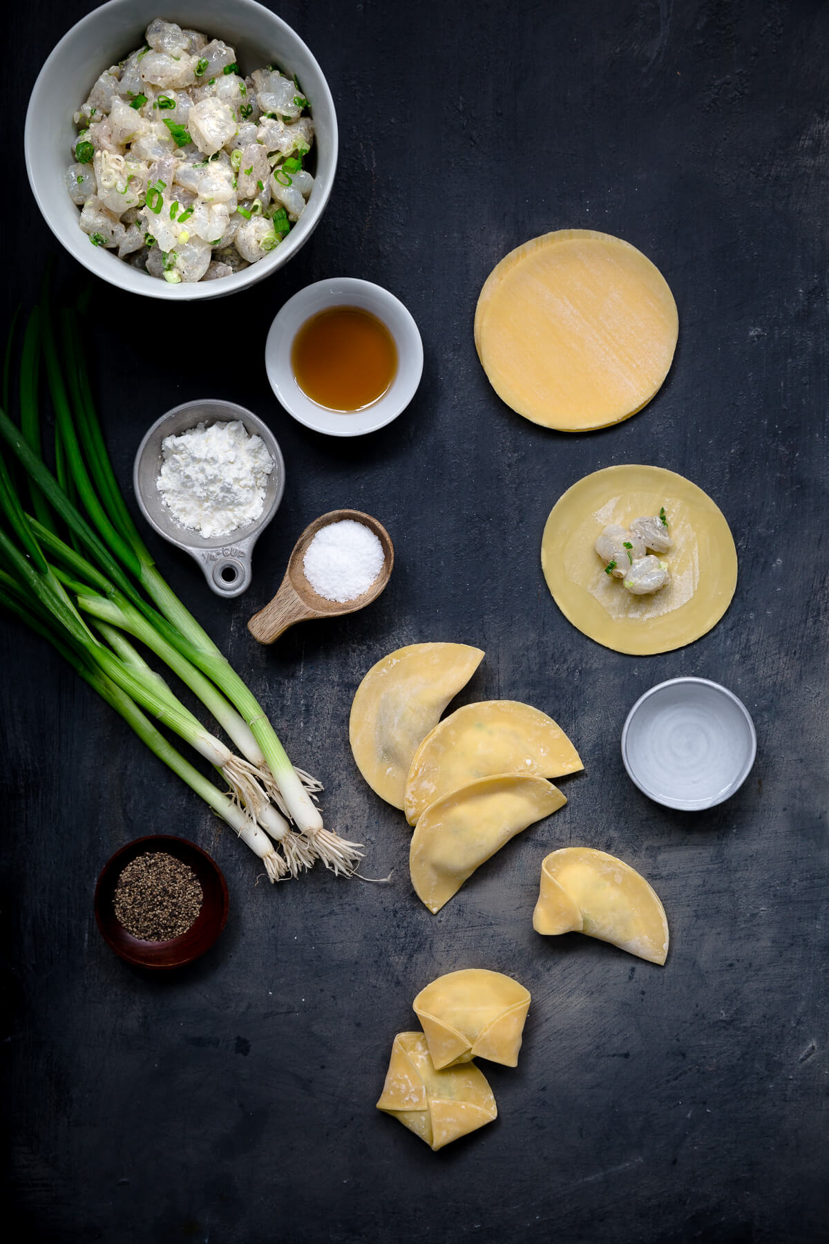 Ingredients for making shrimp dumplings set out on a dark gray board.