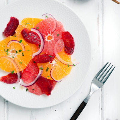 Overhead shot of a citrus salad with grapefruit, blood oranges, and navel oranges on a white plate.