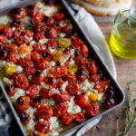 A baking tray of roasted tomatoes and feta topped with olive oil and thyme.