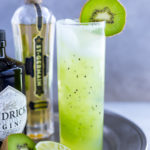 Kiwi cocktail in a tall garnished with a fresh kiwi slice.