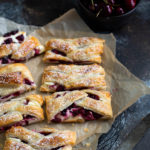 Several slices of cherry cream cheese danish on brown parchment paper.