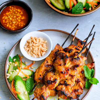 Overhead view of skewers of chicken satay served with a cucumber salad.