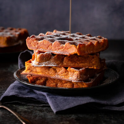 Syrup being poured on a stack of pumpkin spice waffles.