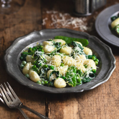 A plate of lemon gnocchi with spinach and peas on a wooden tabletop.