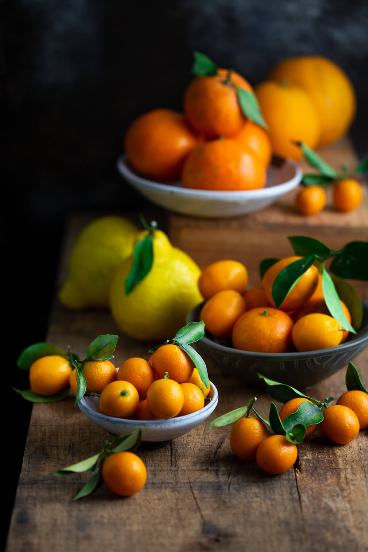 Several bowls of citrus on a wooden tabletop.