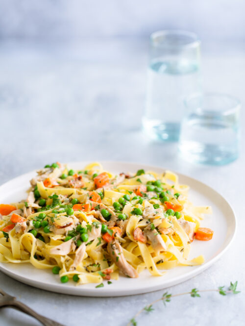 Fettuccine with chicken, peas, and carrots on a white plate.