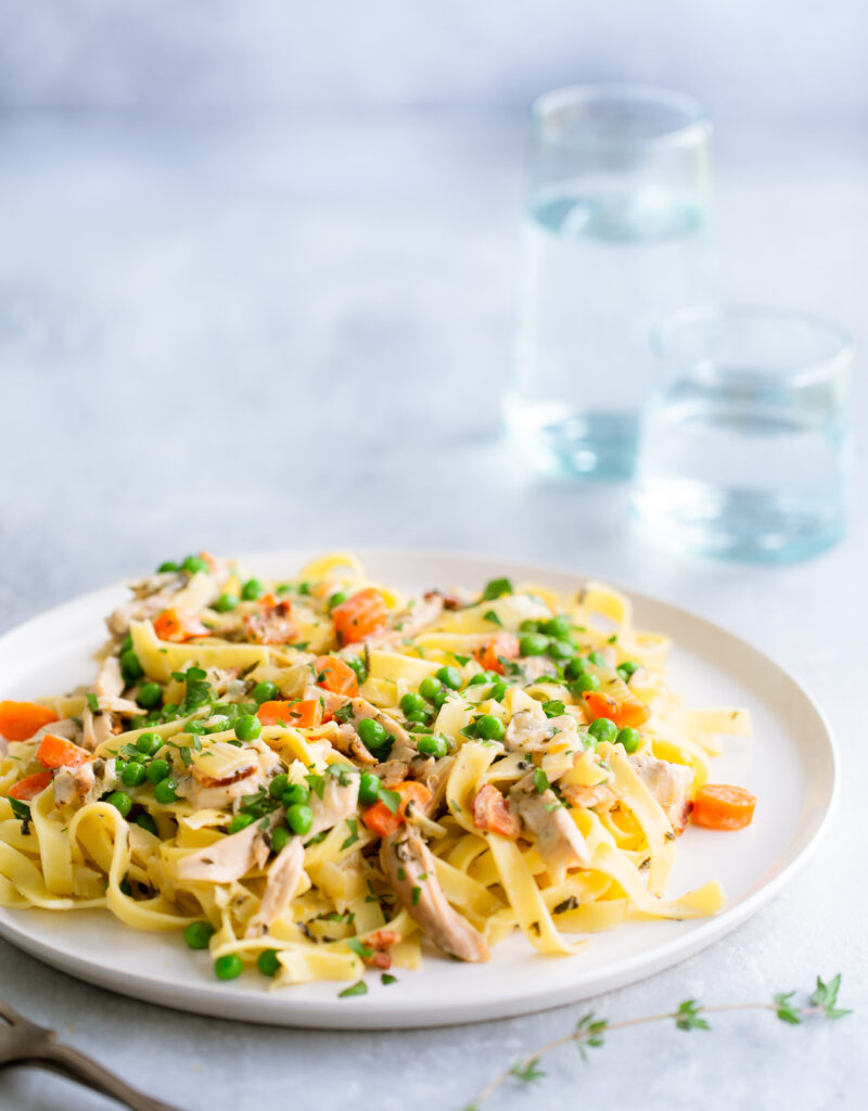 Fettuccine with chicken, peas, and carrots on a white plate.