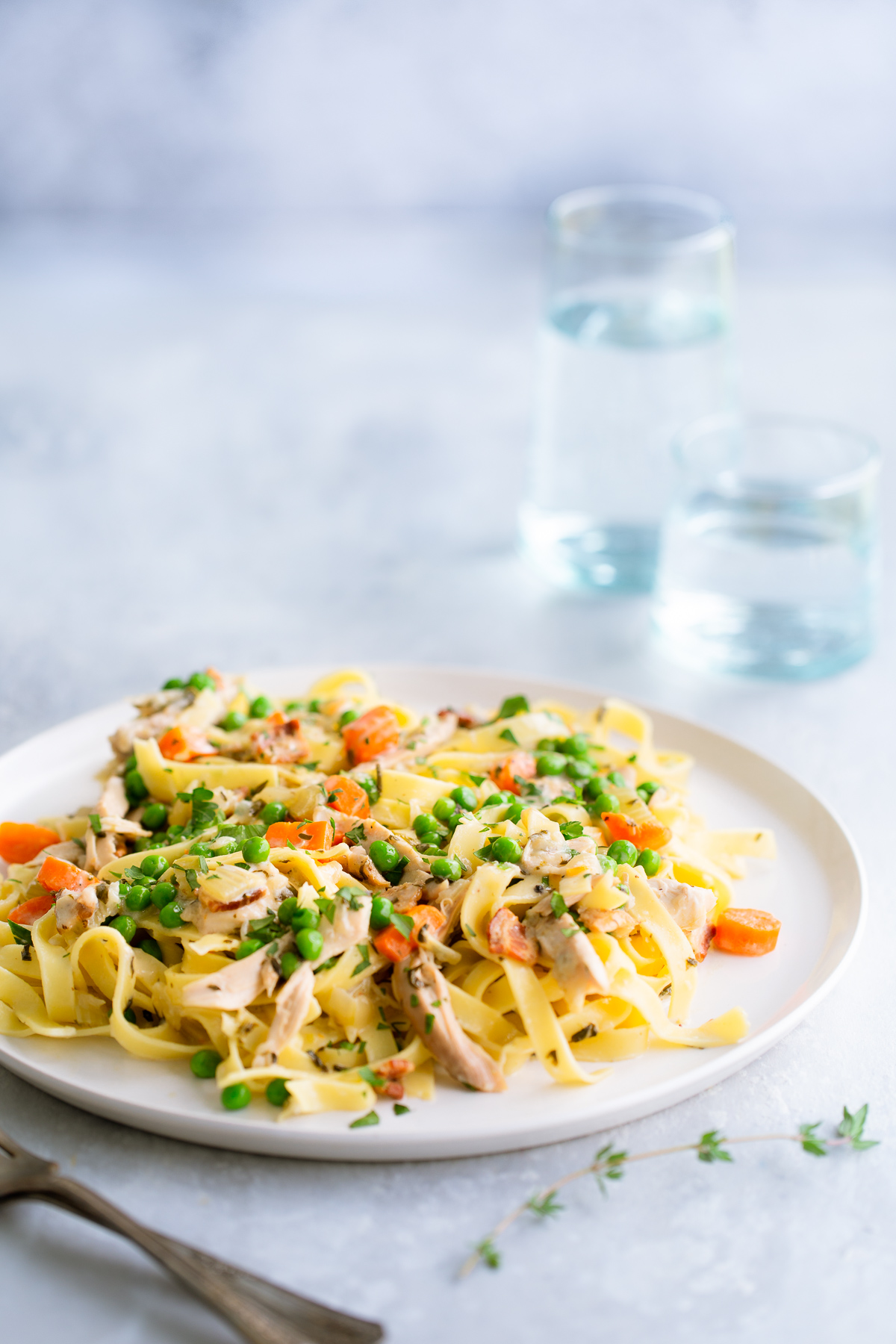 Fettuccine with chicken, peas, and carrots on a white plate.