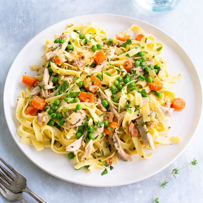 Fettuccine with chicken, peas, and carrots on a white plate.