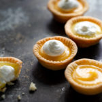 Close-up of several lemon tartlets topped with whipped cream on a tabletop.