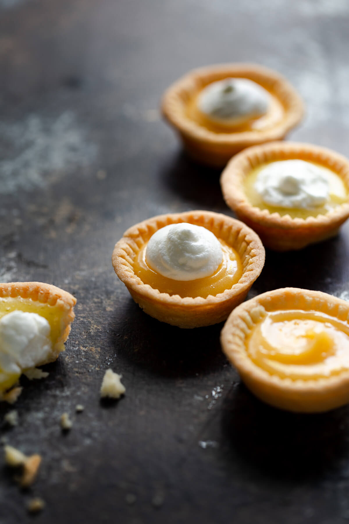 Close-up of several lemon tartlets topped with whipped cream on a tabletop.