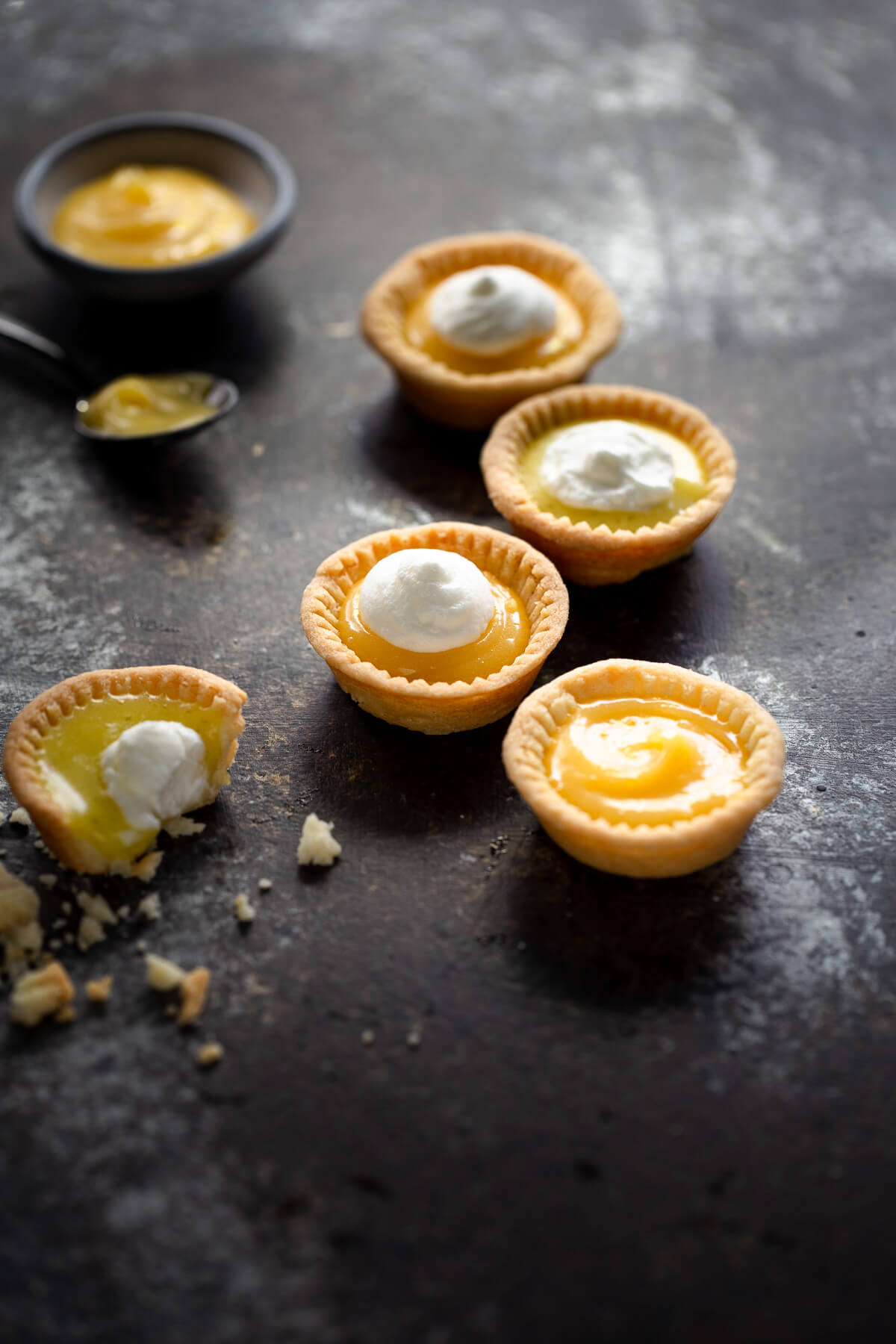 Several lemon tartlets topped with whipped cream on a tabletop.