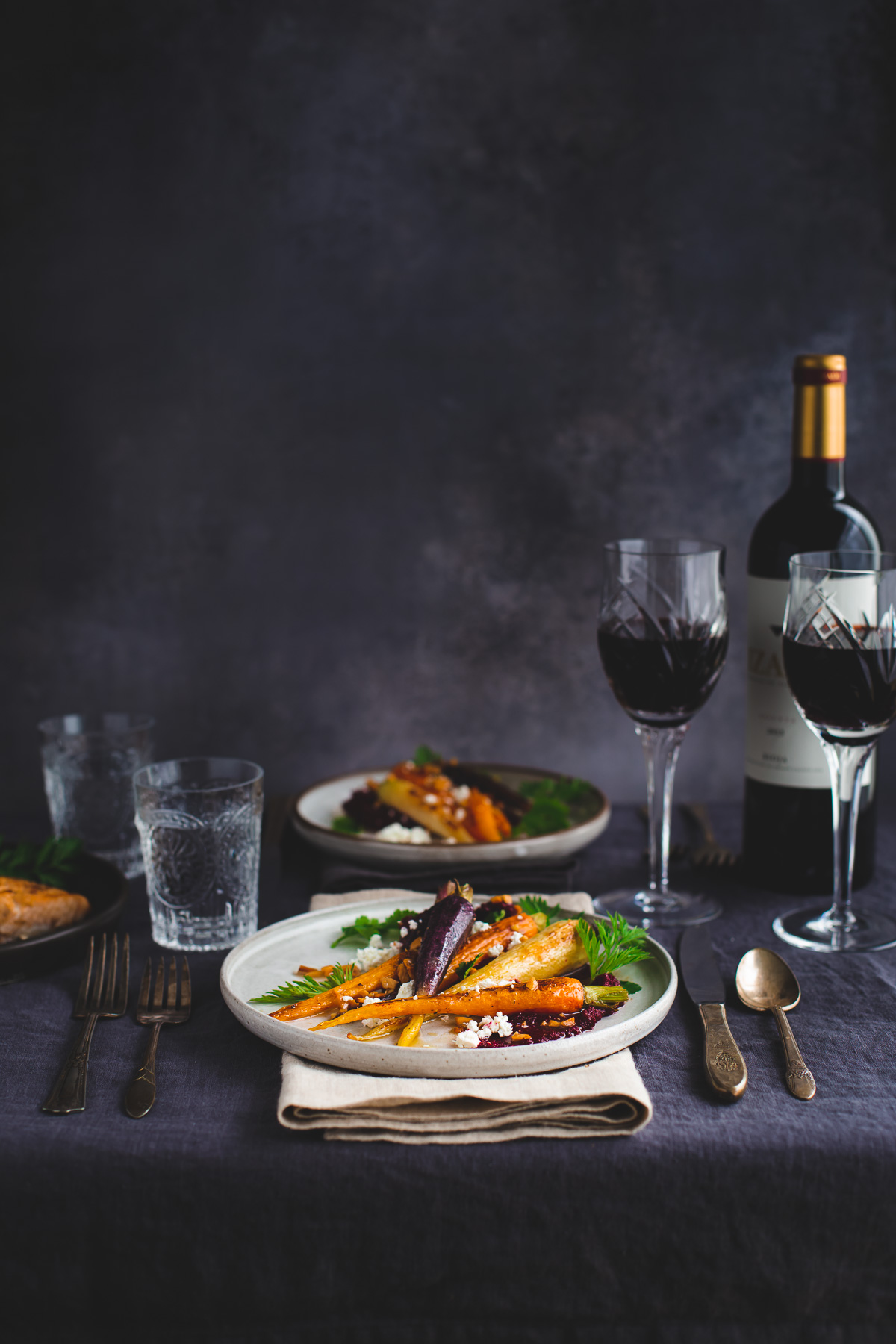 Plates of roasted carrots on a linen tablecloth.