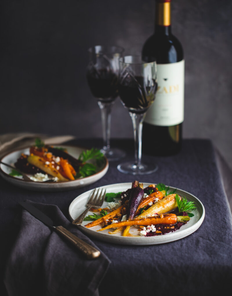 Plates of roasted carrots with beet purée next to wine glasses.