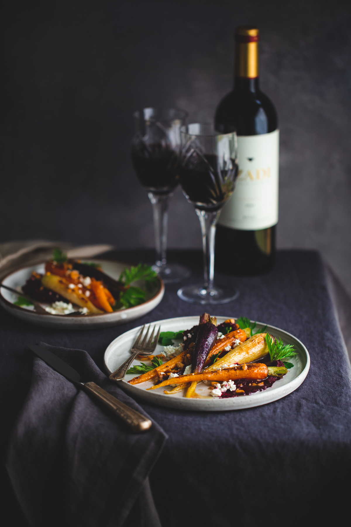 Plates of roasted carrots with beet purée next to wine glasses.