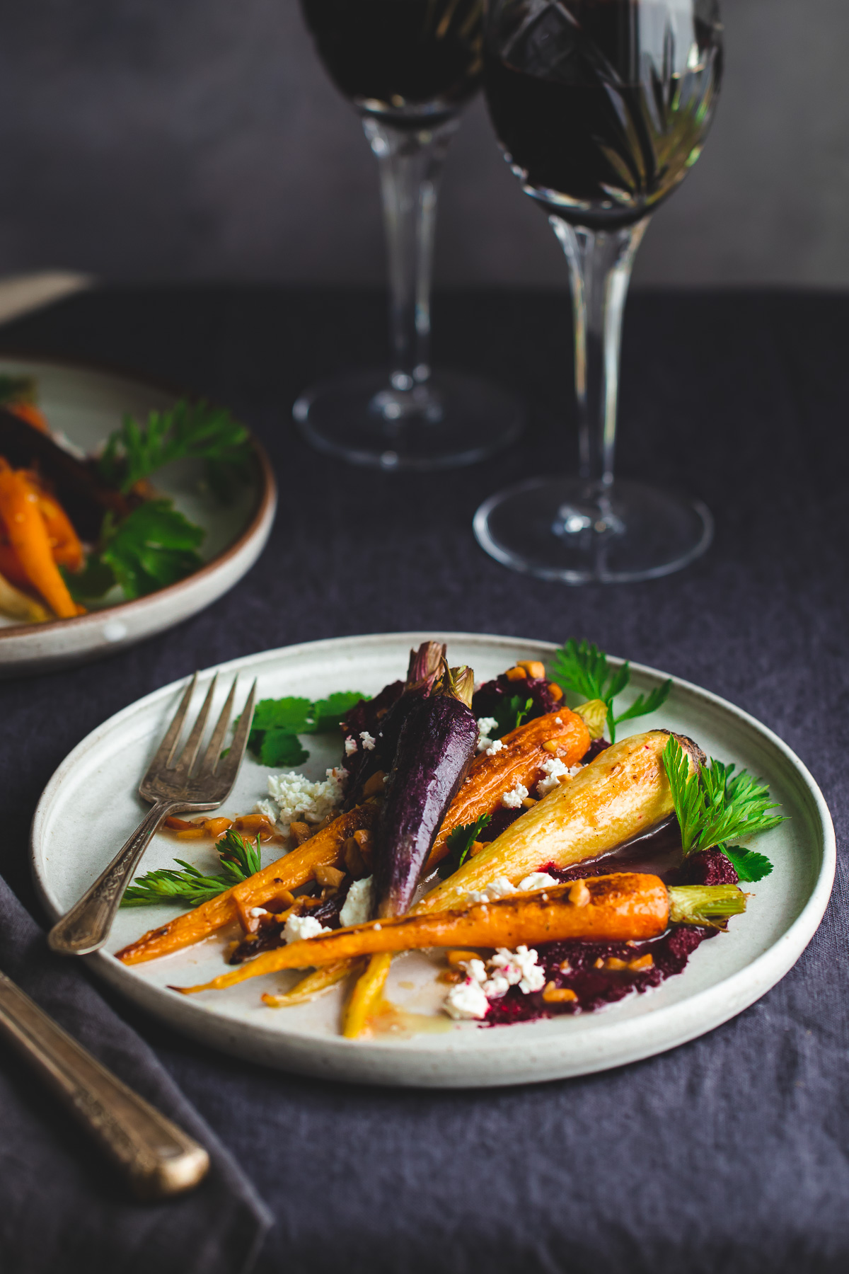 Plate of roasted carrots with beet purée topped with crumbled feta and carrot leaves.