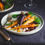 Plate of roasted carrots with beet purée topped with crumbled feta and carrot leaves.