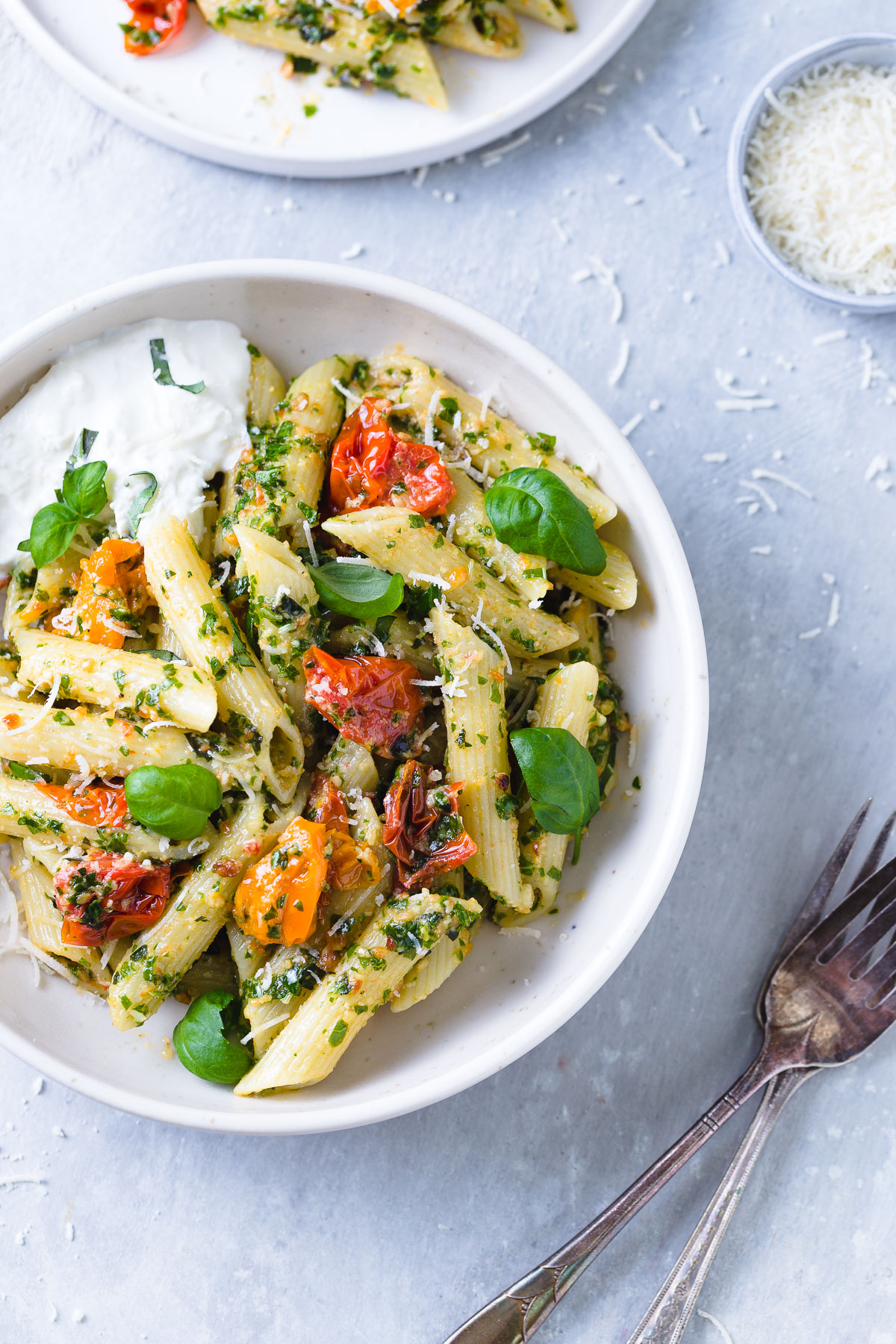 Penne tossed with kale pesto and roasted tomatoes and a serving of burrata cheese in a white bowl.