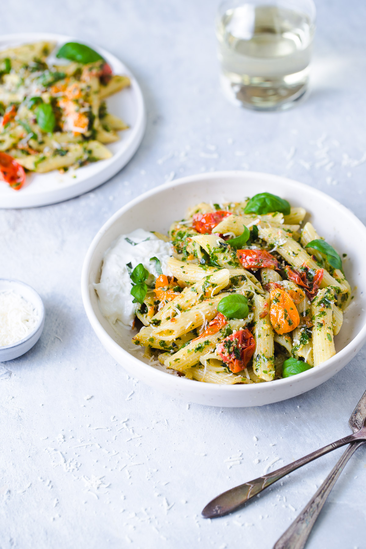 Penne tossed with kale pesto and roasted tomatoes and a serving of burrata cheese in a white bowl.