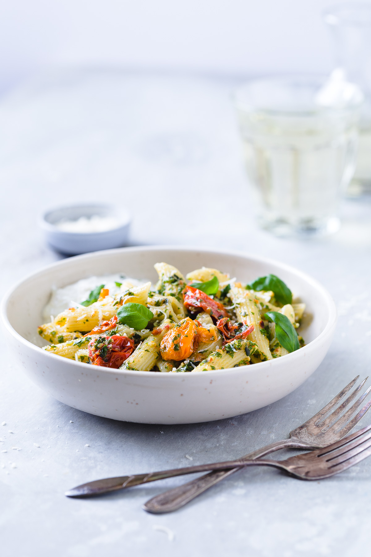 Penne tossed with kale pesto and roasted tomatoes and a serving of burrata cheese in a white bowl.