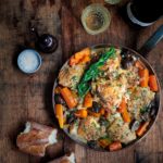 Braised chicken and carrots in a pan on a wooden surface with white wine and a baguette.