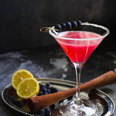Blueberry Lemon Drop cocktail in a tall martini glass garnished with blueberries on a metal tray.