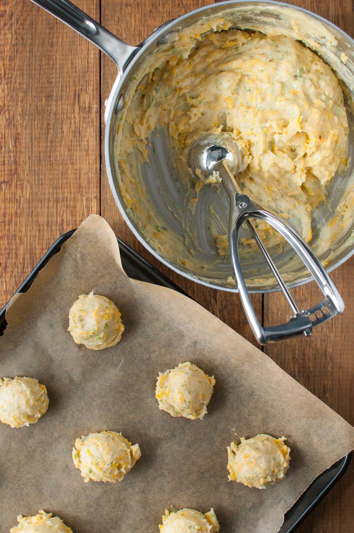 Dough for cheddar dill puffs in a saucepan and scoops of dough on a baking sheet.