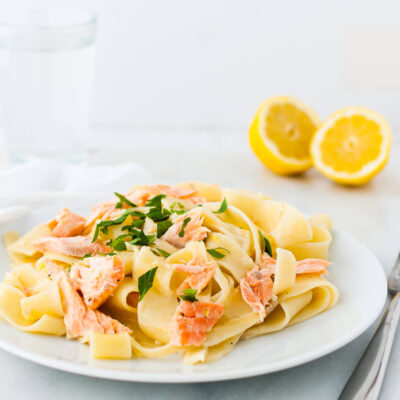 Lemon pasta with salmon garnished with chopped parsley on a white plate.